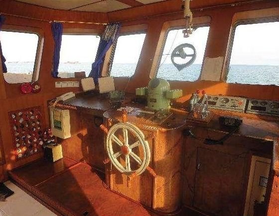 Wheelhouse of a THS vessel with a wooden helm, navigation panel, and windows facing the sea