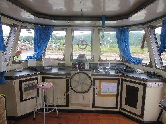 Wheelhouse of a THS vessel with a helm, white control panels, and windows overlooking a riverbank