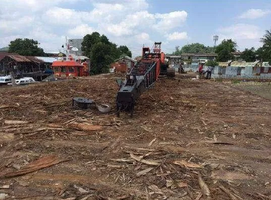 Barge deck with timber log debris and heavy equipment, a tug boat in the background