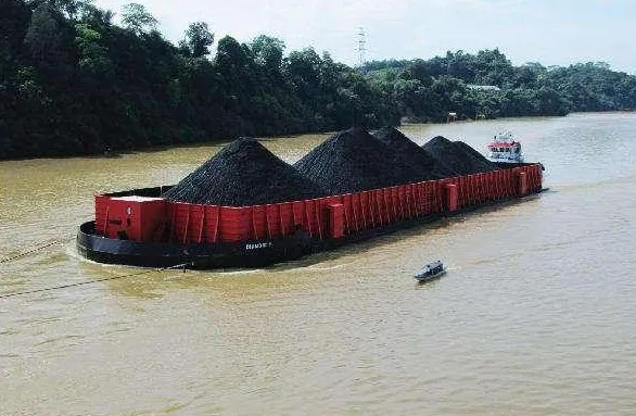 Coal-laden barge towed by a tug boat on a river