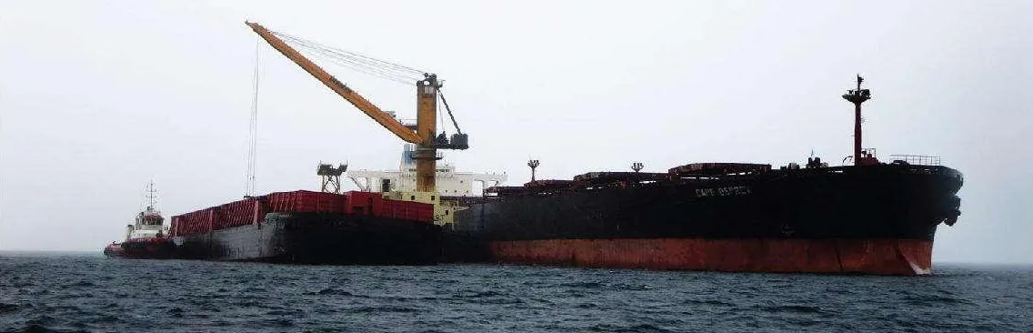 Barge moored alongside a bulk carrier while the ship crane transfers cargo