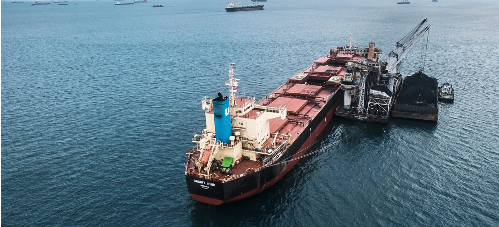 Coal-laden barge and tug boat alongside a bulk carrier during cargo transfer at sea